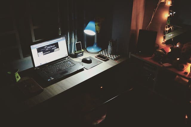 Cozy office with laptop, desk lamp, and personal decor at night.