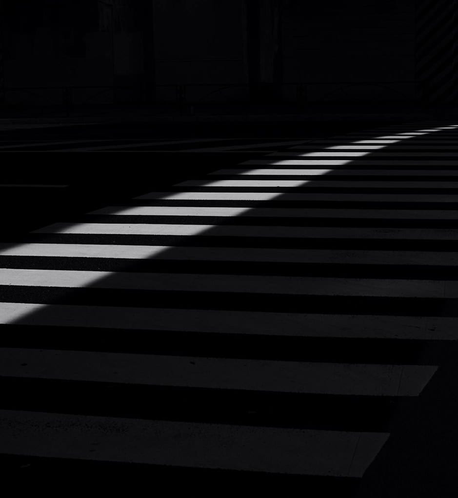 Shadowed crosswalk with striped pattern in urban setting.