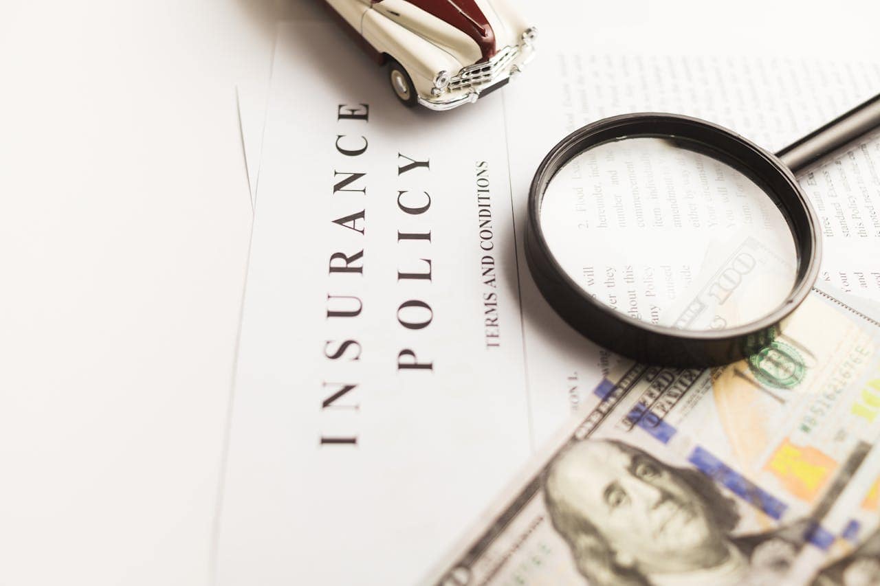 Insurance policy document with magnifying glass, model car, and money, highlighting insurance and risk management.